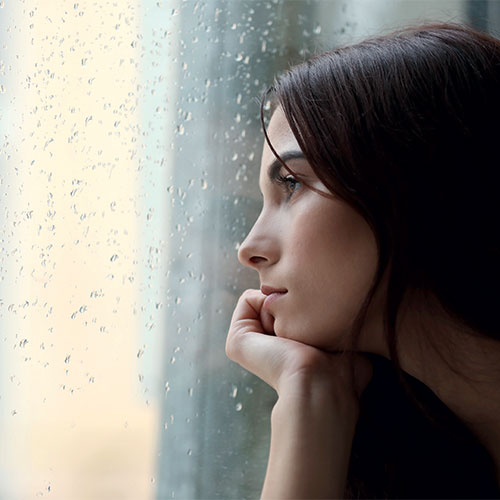 femme regardant par la fenêtre avec un air triste